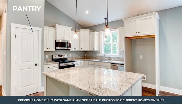 kitchen featuring lofted ceiling, appliances with stainless steel finishes, hanging light fixtures, white cabinetry, and a sink