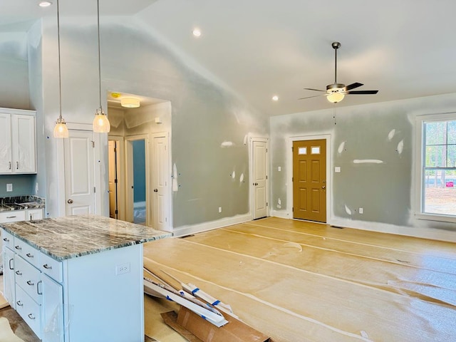 kitchen featuring light stone counters, a center island, white cabinets, baseboards, and hanging light fixtures