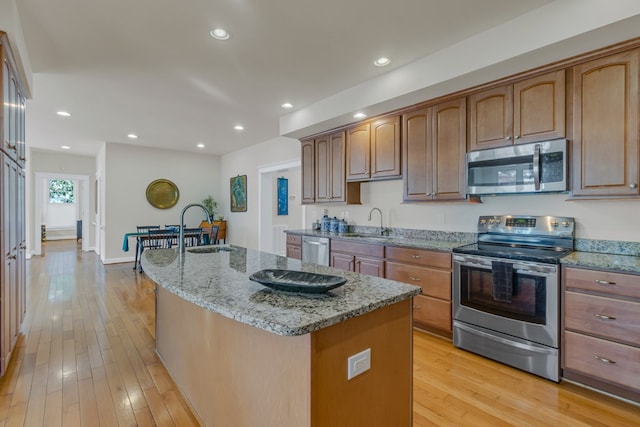 kitchen featuring light wood-type flooring, a sink, light stone counters, an island with sink, and appliances with stainless steel finishes