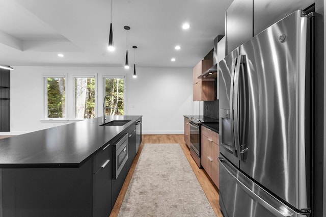 kitchen featuring stainless steel appliances, sink, decorative light fixtures, light hardwood / wood-style flooring, and an island with sink