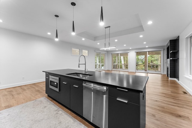 kitchen with sink, an island with sink, pendant lighting, a tray ceiling, and appliances with stainless steel finishes