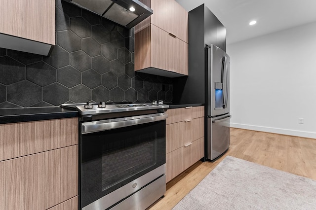 kitchen with backsplash, light hardwood / wood-style flooring, wall chimney exhaust hood, light brown cabinetry, and stainless steel appliances