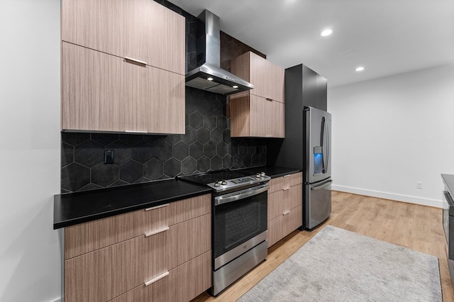 kitchen featuring light brown cabinets, wall chimney exhaust hood, decorative backsplash, light hardwood / wood-style floors, and stainless steel appliances