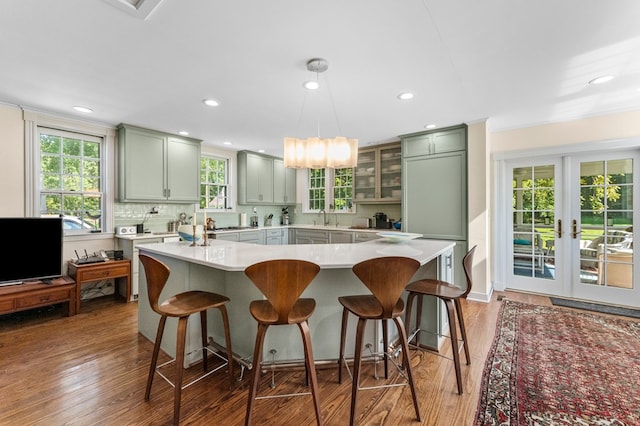 kitchen with dark wood-type flooring, hanging light fixtures, tasteful backsplash, green cabinets, and plenty of natural light