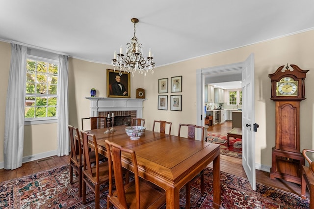 dining room featuring hardwood / wood-style floors, crown molding, a fireplace, and an inviting chandelier