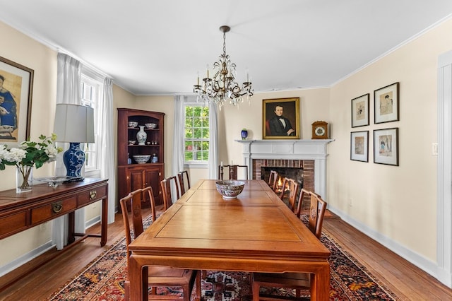 dining room featuring crown molding, a fireplace, hardwood / wood-style floors, and a notable chandelier