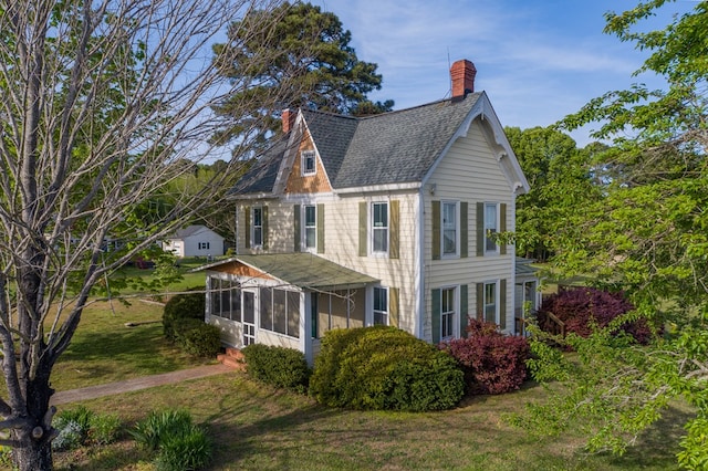 view of property exterior featuring a shingled roof, a yard, a chimney, and a sunroom