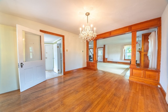 unfurnished room featuring baseboards, light wood finished floors, and a notable chandelier