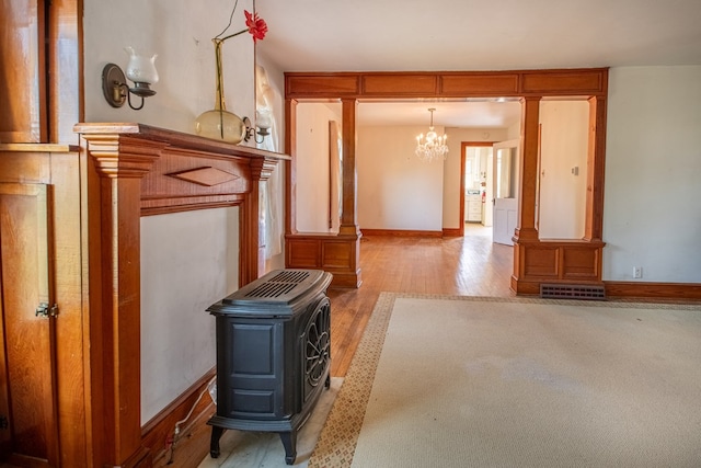 living room featuring visible vents, a wood stove, wood finished floors, baseboards, and an inviting chandelier