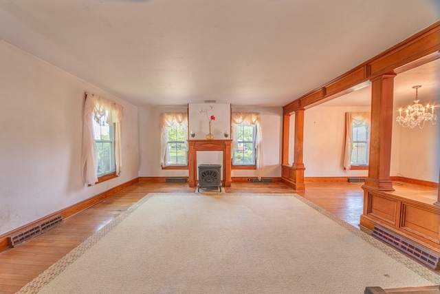 unfurnished living room featuring baseboards, wood-type flooring, decorative columns, and visible vents