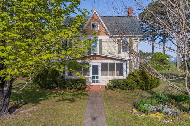 view of front of property with a sunroom, a front lawn, a chimney, and entry steps