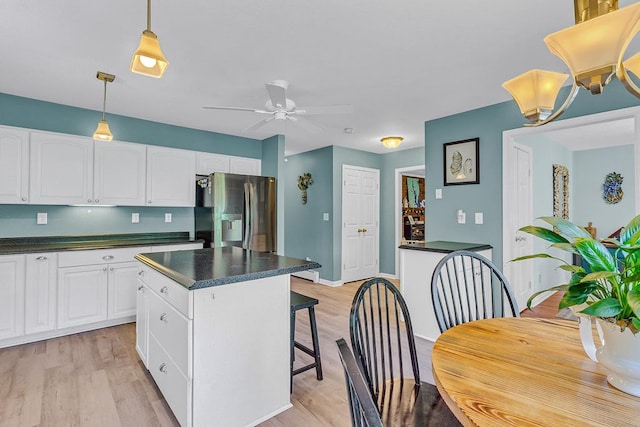 889 Taylors Creek Rd, Weems, VA 22576 - kitchen featuring stainless steel fridge with ice dispenser, dark countertops, light wood-type flooring, white cabinetry, and a kitchen breakfast bar
