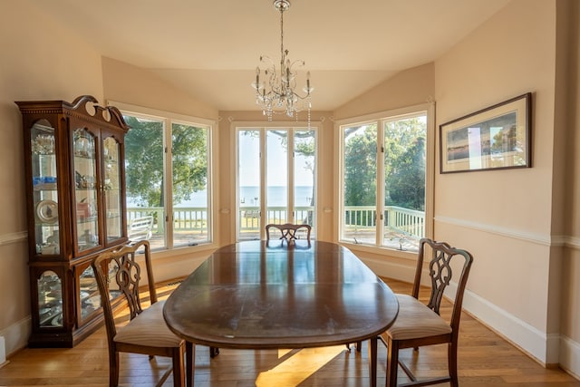 dining space featuring hardwood / wood-style floors, vaulted ceiling, a water view, and an inviting chandelier