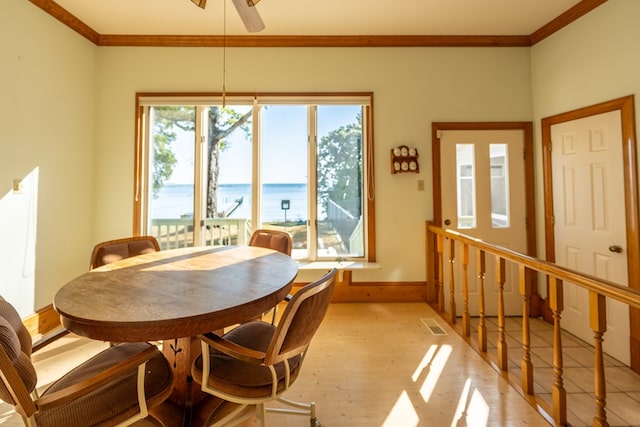 dining space featuring ceiling fan, light hardwood / wood-style floors, a water view, and crown molding