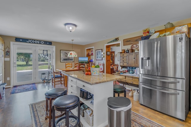 kitchen featuring white cabinets, stainless steel fridge, light stone countertops, decorative light fixtures, and a kitchen island