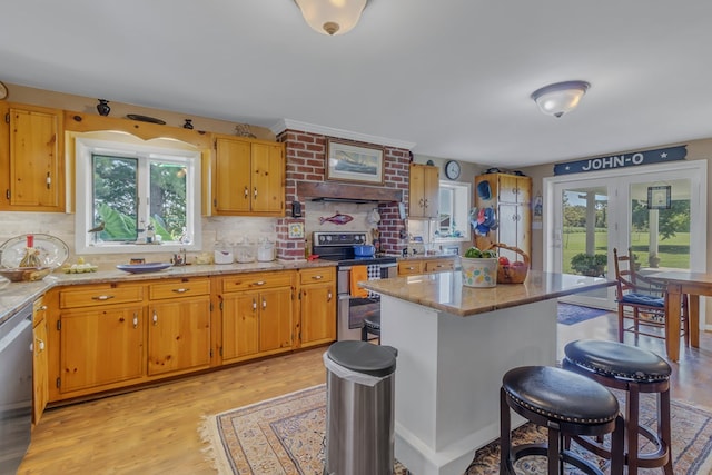 kitchen featuring light stone counters, backsplash, appliances with stainless steel finishes, and light hardwood / wood-style flooring