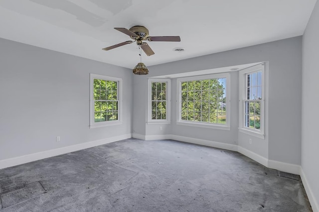 unfurnished room featuring ceiling fan, dark carpet, and plenty of natural light