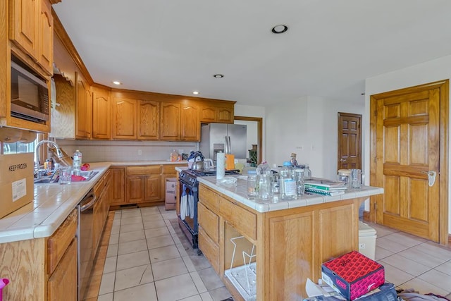 kitchen with tile countertops, a center island, sink, light tile patterned floors, and stainless steel appliances