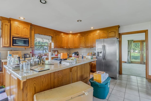 kitchen featuring tile countertops, a healthy amount of sunlight, light tile patterned floors, and stainless steel appliances