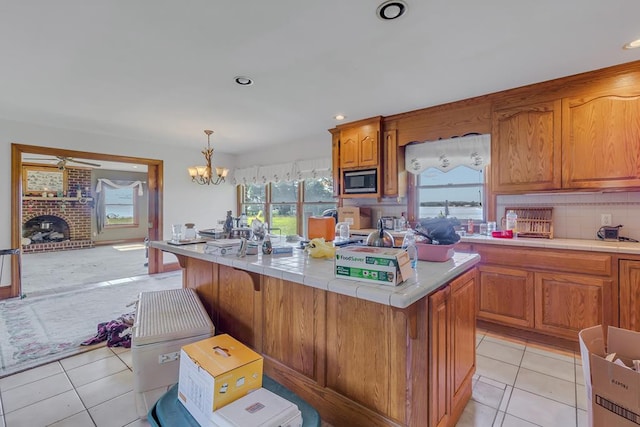 kitchen featuring a center island, stainless steel microwave, hanging light fixtures, a brick fireplace, and light tile patterned flooring