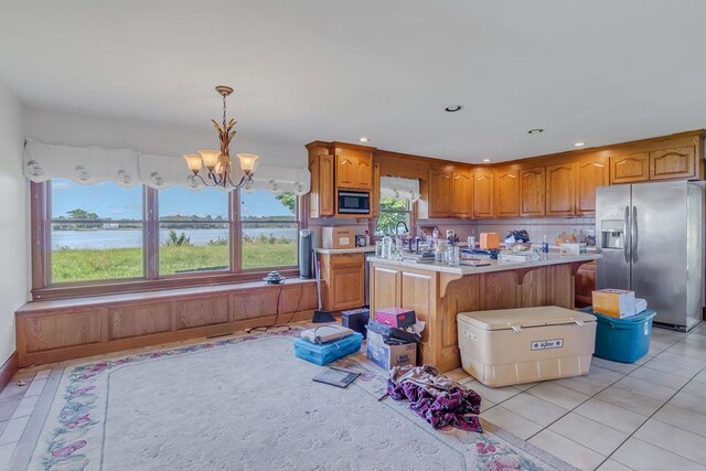 kitchen with appliances with stainless steel finishes, a water view, a chandelier, a kitchen island, and hanging light fixtures