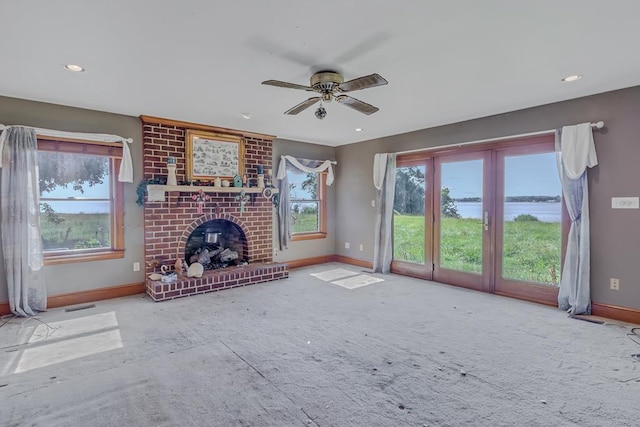 unfurnished living room featuring ceiling fan, a water view, a fireplace, and a wealth of natural light