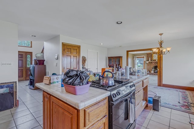 kitchen with tile counters, decorative light fixtures, a brick fireplace, a notable chandelier, and gas stove