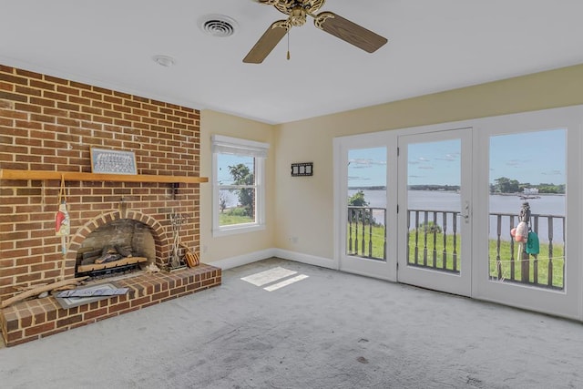 unfurnished living room featuring carpet flooring, ceiling fan, a water view, and a brick fireplace