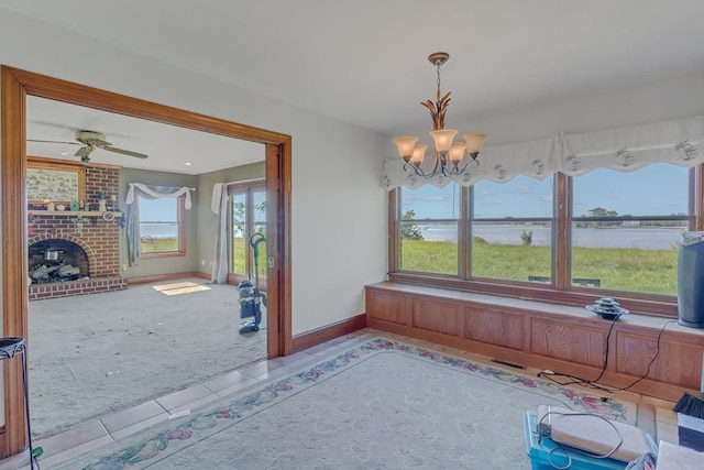 unfurnished dining area with light carpet, a water view, ceiling fan with notable chandelier, and a brick fireplace