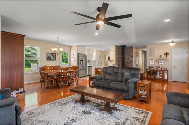 living area featuring ceiling fan with notable chandelier, light wood-style floors, a wood stove, and visible vents