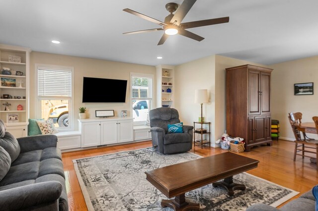 living room with baseboards, built in shelves, recessed lighting, a ceiling fan, and light wood-style floors