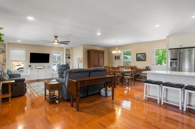 living room featuring ceiling fan with notable chandelier, light wood-type flooring, and recessed lighting