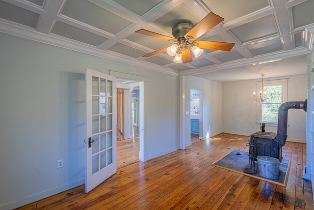 living room featuring hardwood / wood-style floors, ceiling fan with notable chandelier, a wood stove, and coffered ceiling