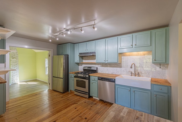 kitchen with light wood-type flooring, tasteful backsplash, stainless steel appliances, sink, and butcher block counters