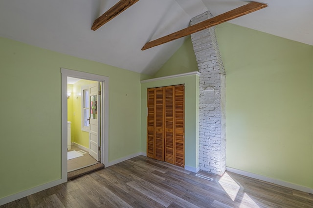 unfurnished bedroom featuring hardwood / wood-style floors, vaulted ceiling with beams, connected bathroom, and a closet