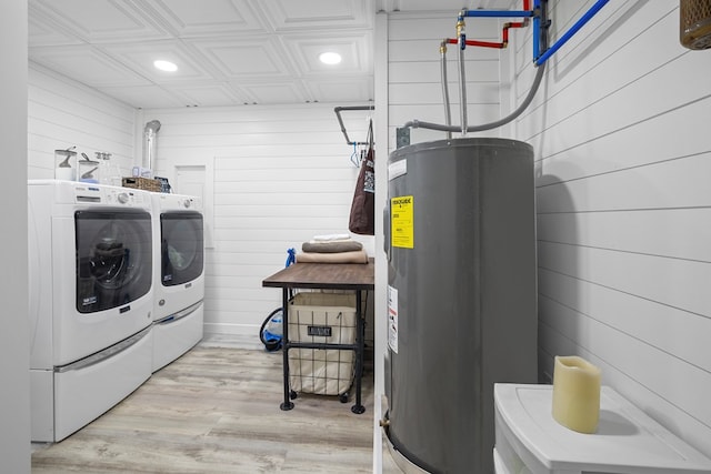 laundry room with water heater, light hardwood / wood-style flooring, washer and dryer, and wooden walls