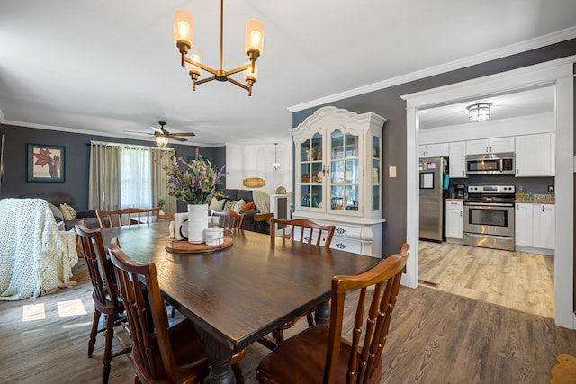 dining space featuring hardwood / wood-style flooring, ceiling fan with notable chandelier, and crown molding