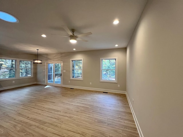 spare room with ceiling fan with notable chandelier, light hardwood / wood-style flooring, and a wealth of natural light