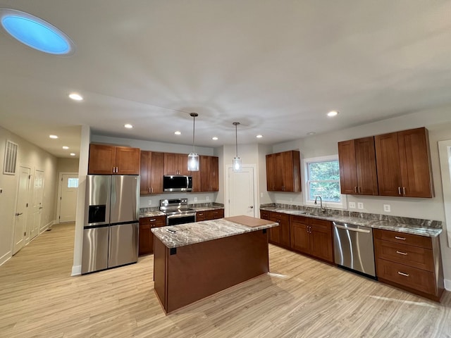 kitchen featuring sink, light hardwood / wood-style flooring, appliances with stainless steel finishes, a center island, and decorative light fixtures