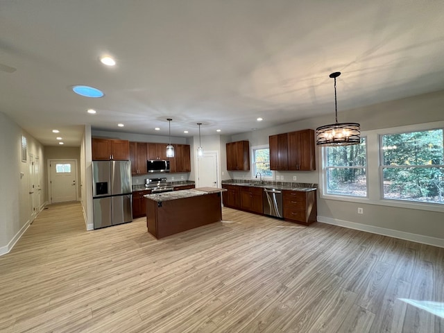 kitchen with light stone counters, a center island, light wood-type flooring, appliances with stainless steel finishes, and pendant lighting