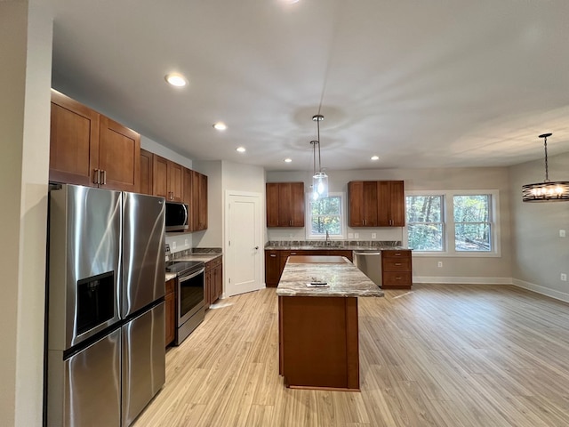 kitchen with appliances with stainless steel finishes, hanging light fixtures, a kitchen island, and light hardwood / wood-style flooring