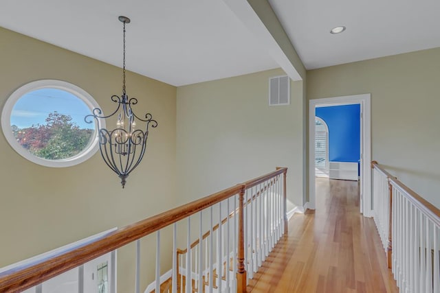 hall with a notable chandelier, light hardwood / wood-style flooring, and beamed ceiling