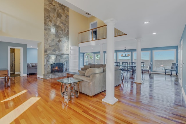 living room featuring a stone fireplace, a high ceiling, light hardwood / wood-style flooring, and ornate columns