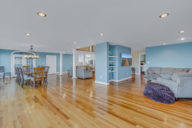 living room featuring built in features, light hardwood / wood-style floors, a chandelier, and ornate columns