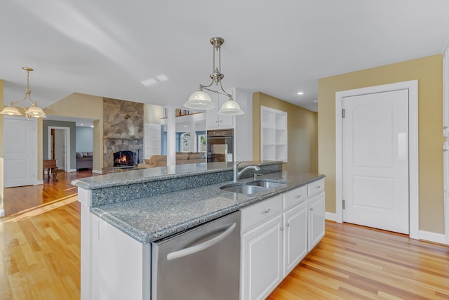 kitchen featuring a stone fireplace, sink, hanging light fixtures, dishwasher, and white cabinets