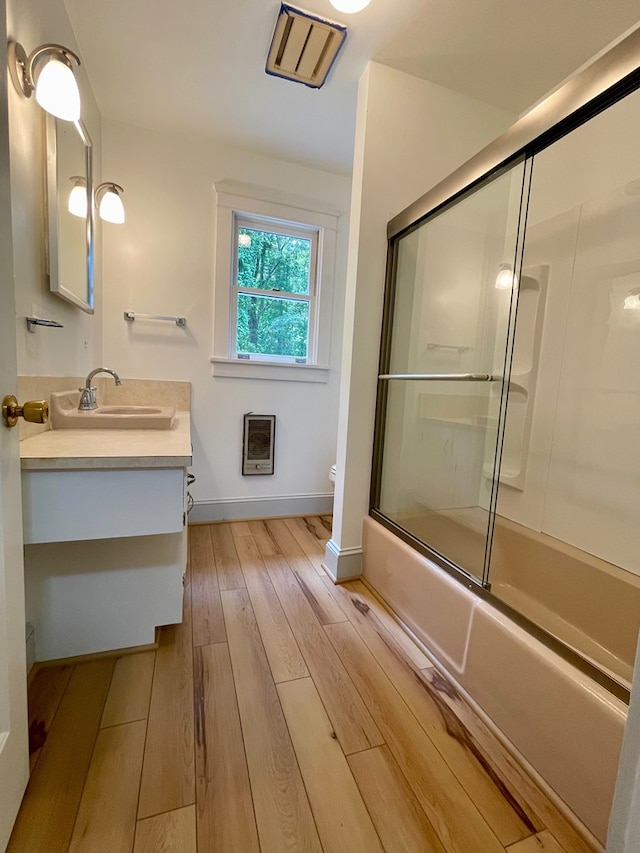 full bathroom with hardwood / wood-style floors, vanity, toilet, enclosed tub / shower combo, and heating unit