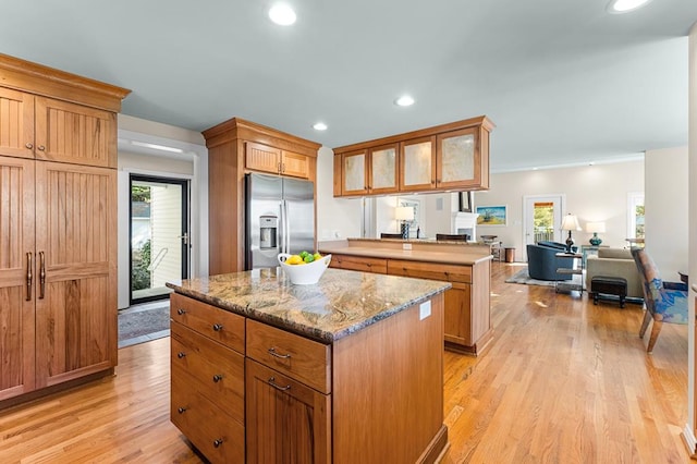 kitchen with light wood-type flooring, a kitchen island, light stone countertops, and stainless steel refrigerator with ice dispenser