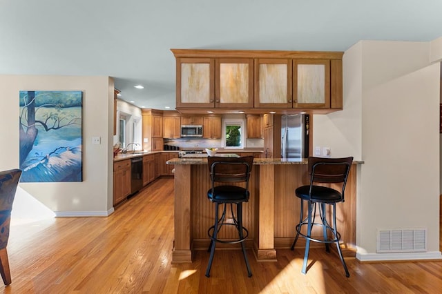 kitchen with stainless steel appliances, kitchen peninsula, light wood-type flooring, stone counters, and a breakfast bar area