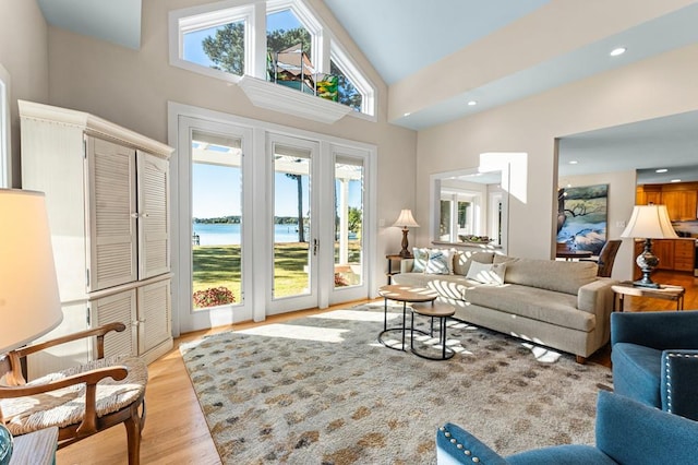 living room with high vaulted ceiling, light hardwood / wood-style floors, and a water view