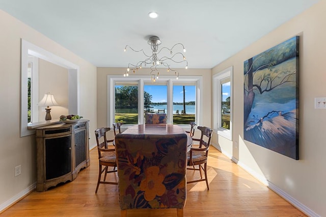 dining area with light hardwood / wood-style floors, a water view, and an inviting chandelier